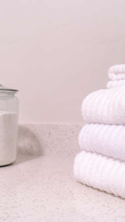 Vertical Folded white towels and glass jar with white powder on the bathroom countertopの写真素材
