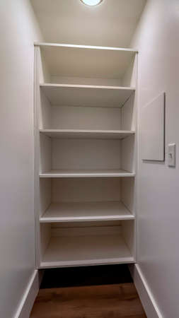 Vertical frame Walk in closet or pantry with empty wall shelves seen through open hinged door. Light switch, in-ceiling round light, and wood floor can be seen inside the storage room.の写真素材