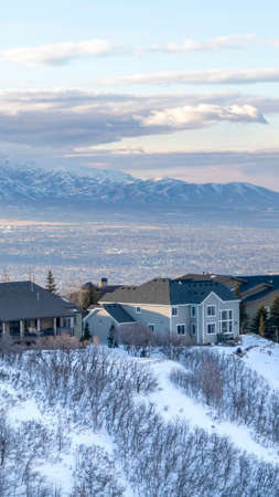Vertical frame Homes in scenic Wasatch Mountains with unobstructed valley and cloudy sky views. The landscape is blanketed with pristine snow during winter season.の写真素材