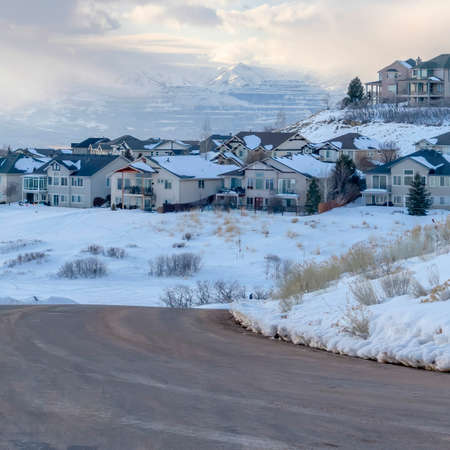 Square frame Curving road on snowy mountain setting with houses against cloudy blue skyの写真素材