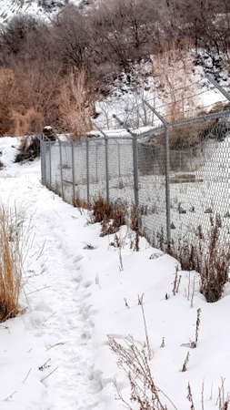 Vertical crop Chain link fence with barbed wires on snow covered hill slope viewed in winter