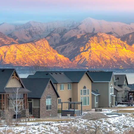 Square frame Homes in the snowy valley with calm lake and golden frosted mountain background. VAst terrain covered with snow and cloudy can also be seen in this beautiful sunset scenery.の写真素材
