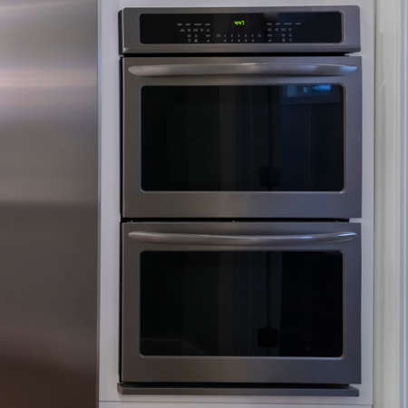 Square Large double door fridge with fitted ovens alongside in a modern home with white cabinets