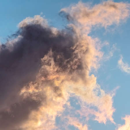 Square frame Grey storm cloud building up at sunset in a sunny blue sky in a background view