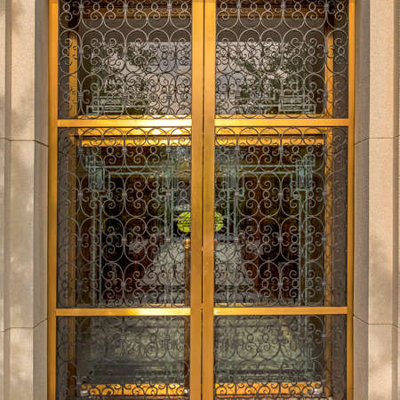 Square crop Decorative wrought iron door with gold frames in front of glass door of building. Building facade with view of the doors at the entrance.の写真素材
