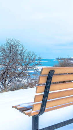 Vertical crop Magnificent scenery at the Utah Lake with an empty bench on the snowy terrainの写真素材