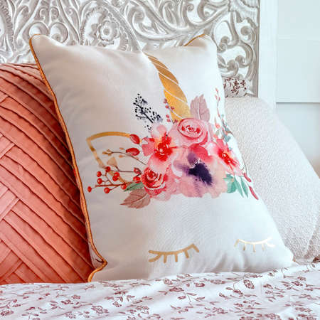 Square crop Fluffy pillows against decorative headboard of single bed against panelled wall. Bedroom interior with an empty bed covered with pink and floral beddings.の写真素材