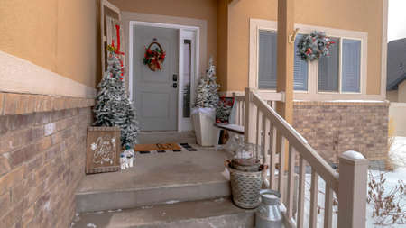 Panorama Wet stairs at home entrance leading to front door with christmas tree and wreath. The yard of the house is covered with snow on this cold winter season.の写真素材