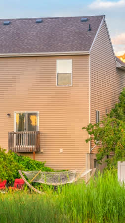 Vertical frame Home amid lush green foliage with cloudy blue sky and sunlit mountain backgroundの写真素材