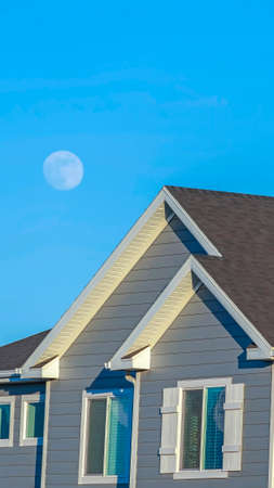 Vertical crop Sunlit home with dark pitched roof over horizontal gray wall siding and windowsの写真素材