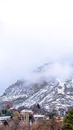 Vertical crop Rocky Provo Canyon in Utah blanketed with thick clouds and dusted with snow. The...