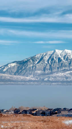 Vertical frame Picturesque Wasatch Mountains and Utah Lake under cloudy blue sky in winter. Houses with view of the scenic nature landscape can be seen at the lakefront.の写真素材