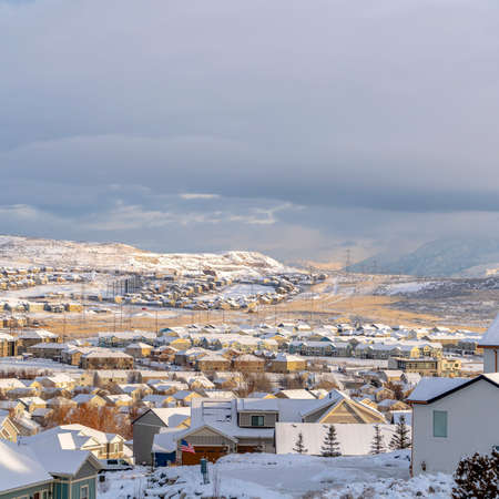 Square frame Homes in snowy Utah Valley neighborhood with scenic view of distant mountain. Thick gray clouds cover the vast sky on this cold day.の写真素材