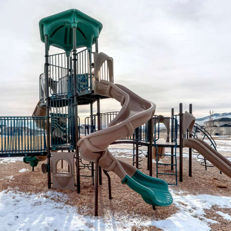 Square frame Slides on a playground with snow on the ground against homes and snowy mountain. AVst...