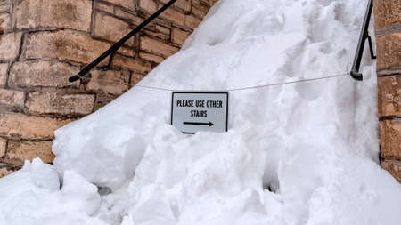 Panorama Snowed in stairs amid stone retaining wall with home and cloudy sky backgroundの写真素材