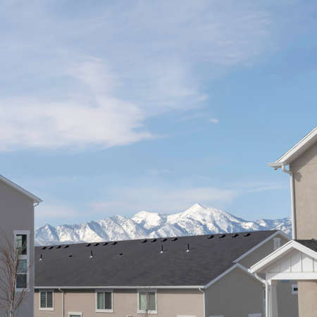 Square Homes in South Jordan Utah with snowy peak of Wasatch Mountains background. Cloudy blue sky is over the neighborhood on a sunny winter day.の写真素材