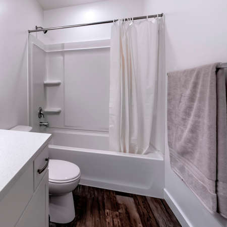 Square Clean white bathroom interior with oval sink mirror toilet bathtub and shower. Gray towel, metal rod, wooden floor, and curtain can also be seen inside the room.の写真素材