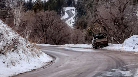 Panorama Road winding through snowy mountain with leafless trees and evergreens in winter. A vehicle is parked on the snow covered side of the road.の写真素材