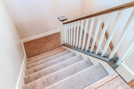 Interior staircase with U shaped design wooden handrail and carpet on treads