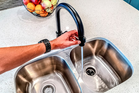 Man holding black curved faucet with water running down the double basin sinkの写真素材