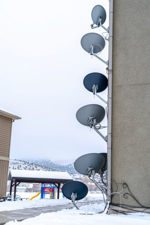 TV satellite dishes on the exterior wall of a building against snowy landscapeの写真素材