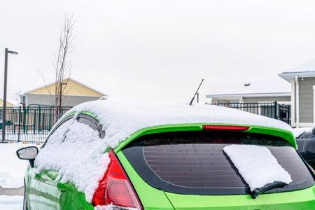 Bright yellow green car covered with snow against homes and sky in winterの写真素材