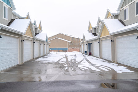Wet and snowy road with tire tracks along white garage doors of apartmentsの写真素材