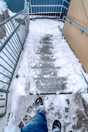 Feet of man on stairway at the side of a building covered with snow in winter