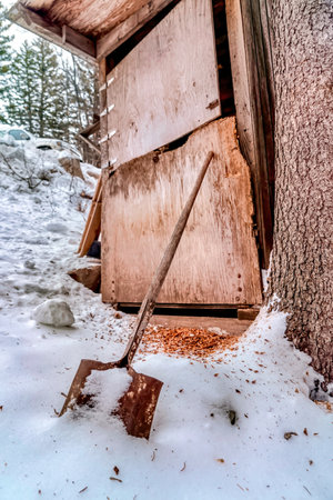 Old shed on snow covered hill with rusty shovel against battered wooden wallの写真素材