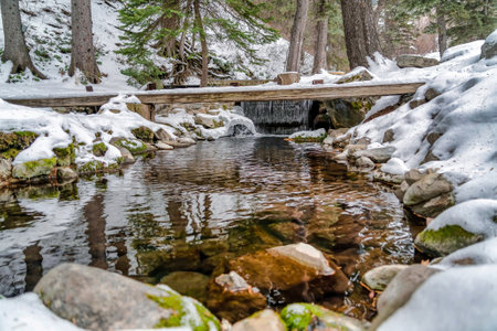 Clear stream water with huge rocks underneath surrounded by snowy nature viewsの写真素材