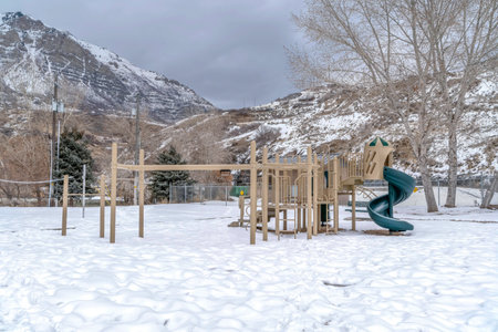 Playground with spiral slide against mountain with ice on a cloudy winter day