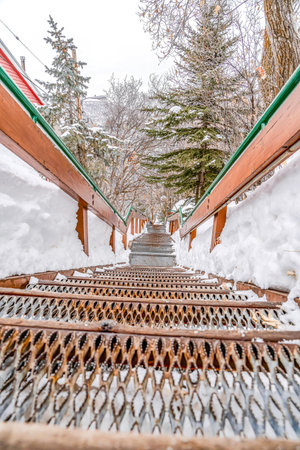 Outdoor mountain stairway with metal treads and handrails against snow and treesの写真素材