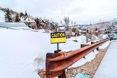 Caution sign on the rusty guardrail of a road in the snowy mountain in winterの写真素材