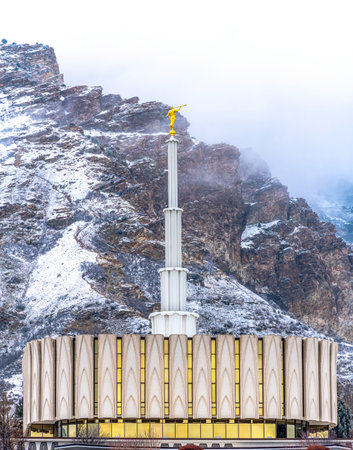 Church exterior with golden statue and white spire against snowy mountain viewの写真素材