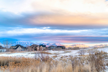 Sunset view of snowy valley in winter with homes against sunlit frosted mountainの写真素材