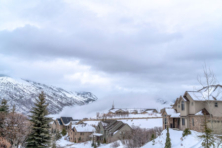Snow covered mountainscape with houses on the slopes under cloudy sky in winterの写真素材