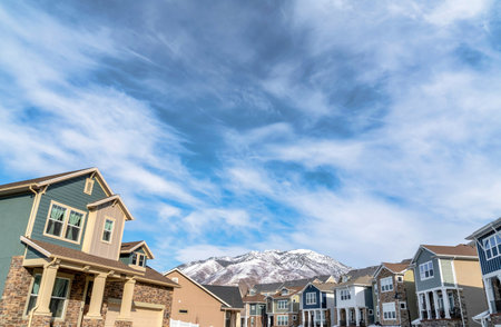 Houses facade with snowy mountain peak and cloudy blue sky on a winter landscapeの写真素材