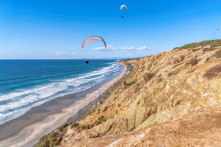 Parachuters flying over scenic beach against blue sky in San Diego Californiaの写真素材