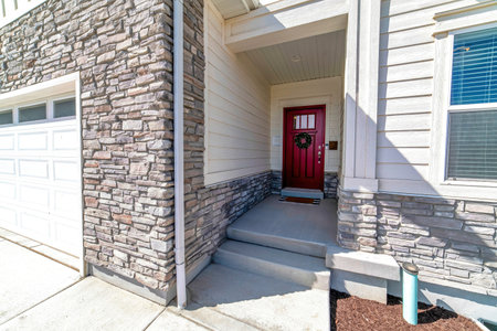 House facade with vibrant red front door attached garage and stone brick wallの写真素材