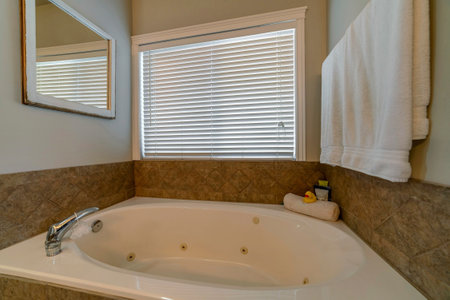 Clean bathtub inside a bathroom with warm toned tiles and white paint on wall