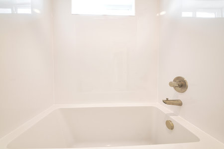Clean bathroom with sparkling built in bathtub and shiny white tiles in the wall