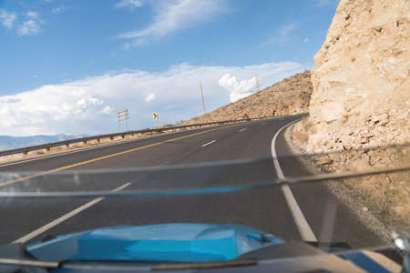Driving on a curved uphill road beside a rocky mountain in Hurricane, Utahの写真素材