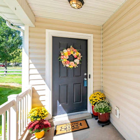 Square frame Front door porch with decorative displays of flower wreath and potted flowers at the floorの写真素材