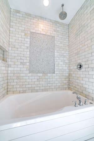 Alcove bathtub with marble subway tile surround and shower head. There is a mosaic display at the...