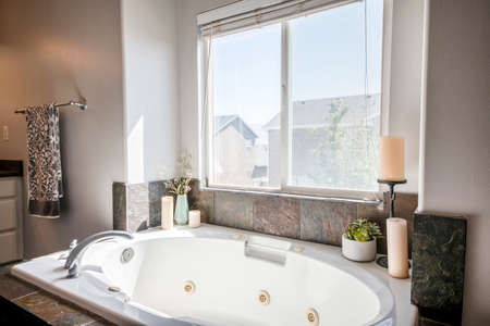 Bathtub with deck mounted faucet and rough stone tiles surround against the windowの写真素材
