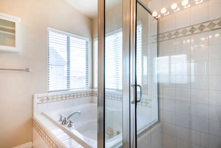 Bathroom interior with bathtub and shower stall with ceramic tiles surround near the windows