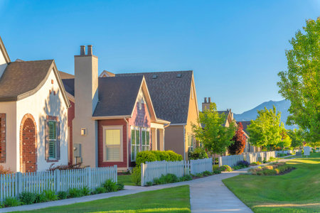 Concrete walkway at the front of houses with picket fence at Daybreak in South Jordan, Utah. Daybreak residences with green front lawn with trees and a view of mountains and sky at the back.の写真素材