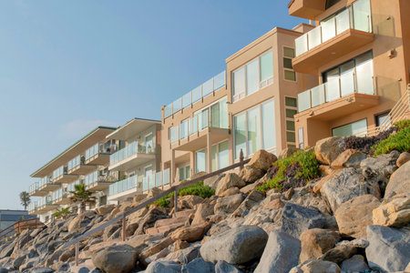 Rocky seawall with wooden handrails near the beachfront buildings at Oceanside, California. Multi-storey buildings exterior with glass railings on decks.の写真素材