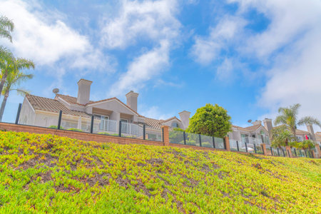 Residential area on top of a grassy slope at Laguna Niguel in Southern California. There is a fence with bricks and glass at the edge of the slope and a background of a sky with clouds.の写真素材