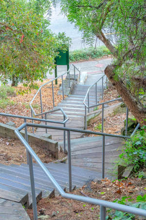 Outdoor staircase on a slope with metal handrails and wooden steps with anti-slip strips